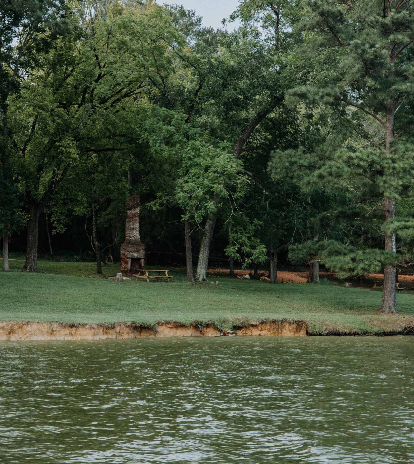 Brick lakeside fireplace set among large trees
